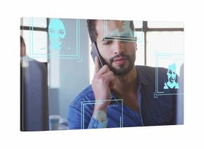 Talking on smartphone Middle Eastern man viewing monitors on office desk, with recognition overlays