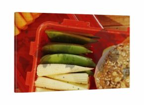 Resting red crate containing baby corn, sugar snap peas and seeded grain bun on kitchen countertop