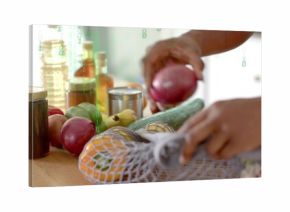 Hands placing red onion into reusable mesh bag on home kitchen countertop, with glass oil jars