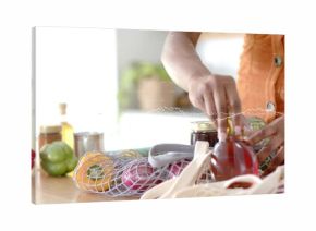 Torso and hands wearing orange top placing honey jar on kitchen counter, mesh bag, copy space