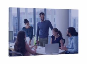 Reviewing plans, team wearing business-casual leaning over meeting table, laptop and safety vests