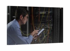 Repairing Korean tech in blue shirt leaning into server rack, using tablet tracing Ethernet cables