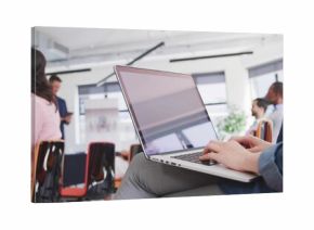 Typing woman in denim jacket using silver laptop on lap in workshop, flip chart, copy space