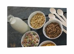 Showcasing five white bowls holding cereals on dark wooden table, with milk bottle and spoons