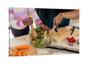 African American mother and daughter mixing salad in glass bowl at counter with wooden spoons
