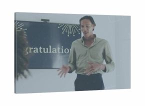 Speaking presenter in green shirt and dark pants in meeting room, with display showing gratulation