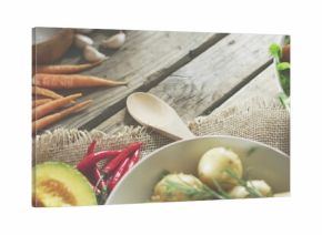Displaying ceramic bowl of new potatoes with herbs on rustic wooden table, with wooden spoon