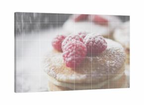 Showing stacked pancakes sitting on soft table in cafe with 3 raspberries powdered sugar doily grid