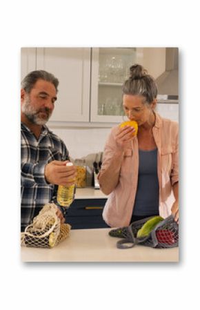 Mature couple in kitchen unpacking groceries, smelling fresh produce together, at home