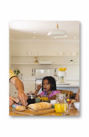 Family enjoying breakfast together at home, father slicing bread, daughter watching
