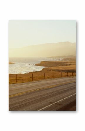 This is Route 1also known as the Pacific Coast Highway. The road is situated next to the ocean with the mountains in the distance. The road goes off into infinity into the sunset.