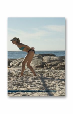 Volleyball player standing ready near yellow net post on sandy beach by rocky outcrop and ocean