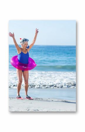 Senior woman raising arms, wearing snorkel mask, breathing snorkel, red fins and pink tube on beach
