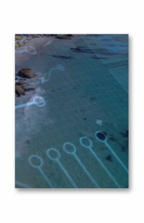Hovering translucent blue circuit grid overlay over beach cove, with umbrellas, boulders and houses