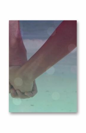 Holding hands of couple wearing light beach shorts, pink sleeveless top in shallow surf, soft flare