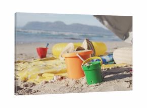 Sitting orange and green sand buckets holding sand on pale beach near shoreline, with towel