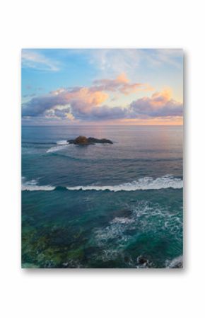 Panoramic view of tropical beach with surfers at sunset.