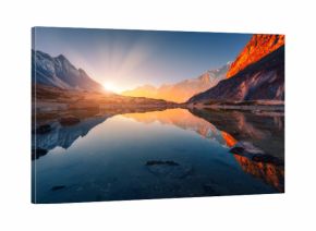 Beautiful landscape with high mountains with illuminated peaks, stones in mountain lake, reflection, blue sky and yellow sunlight in sunrise. Nepal. Amazing scene with Himalayan mountains. Himalayas