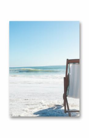 Person relaxing on wooden deck chair at beach shoreline, hand resting on striped seat, copy space