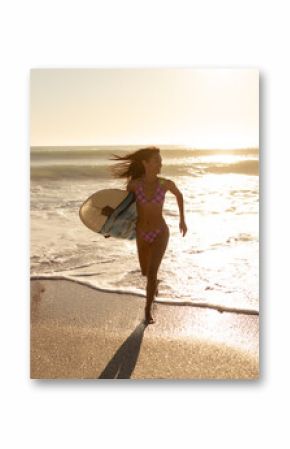 Woman running from breaking waves onto wet sand at beach edge, holding surfboard during golden hour