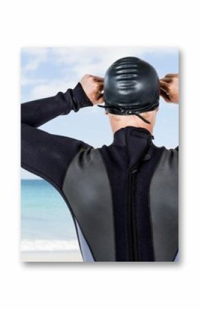 Male swimmer adjusting swimming cap while standing at beach