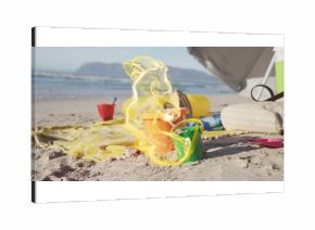 Arranging colorful sand buckets and shovel on sunny beach shore, with striped towel and cooler bag