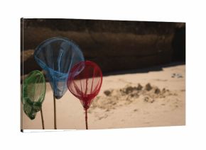 Three multicolored mesh nets are standing in sand on beach near dark rock and sand pile