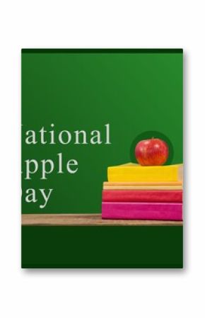 Composite of books and fresh apple on wooden table with national apple day text on green background