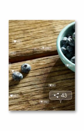 Blueberries are spilling from teal bowl onto a wooden surface