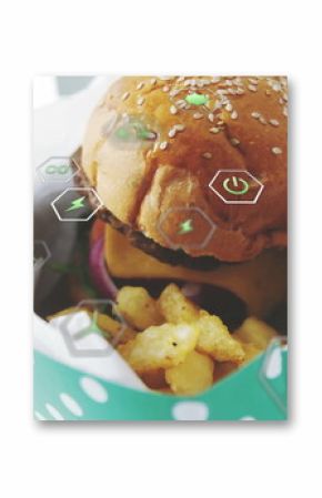 Showing sesame burger with onion and crinkle-cut fries in to-go box on tabletop, with digital icons