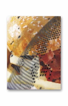 Presenting sesame-seed bacon cheeseburger in cardboard tray, with golden fries and checkered liner