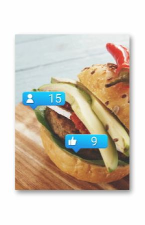 Displaying burger layered with avocado, tomato, lettuce and chili pepper on board, social icons