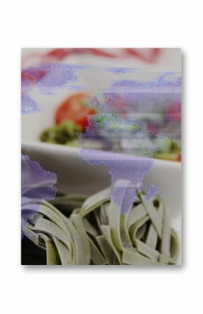 Spinach tagliatelle nests sitting on red-white checkered cloth in kitchen, with salad bowl and fork