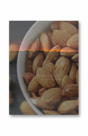 Showing white ceramic bowl holding raw whole almonds on dark grey countertop, copy space