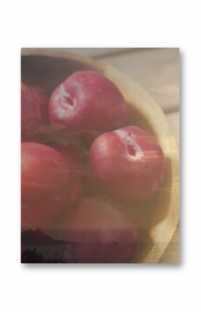 Displaying wooden bowl holding bright red plums on rustic kitchen table, with dewy skins
