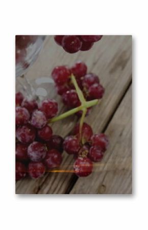 Showing frosted red grapes resting on rustic wooden tabletop, under inverted clear wine glass