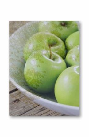 Displaying white ceramic bowl holding shiny green apples on wooden kitchen table, copy space