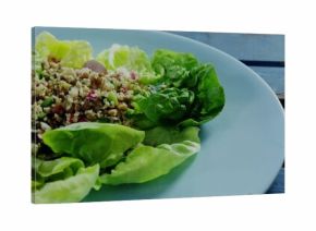 Lettuce leaves holding grain salad with lentils onion herbs on dining table blue plate, copy space