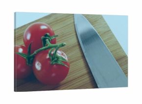 Shining 3 cherry tomatoes with green stems sitting on board in kitchen, serrated knife, copy space