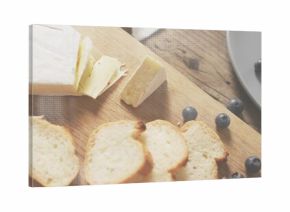 Displaying brie wedge resting on wood cutting board, with toasted crostini and loose blueberries