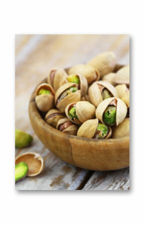 Pistachios with and without shell in bamboo bowl on rustic wooden surface  