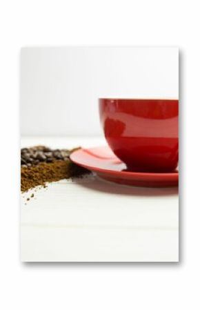 Showing flat-lay red coffee cup resting on wood plank, spilling roasted beans and coffee grounds