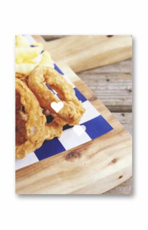 Showing onion rings, crinkle-cut fries and burger on board with checked paper on table, copy space