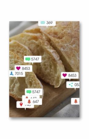 Partially sliced baguette resting on wooden cutting board on grey tabletop, with notification icons