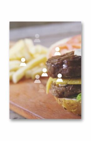 Drizzling sauce onto double cheeseburger with fries on wooden board, icons floating, copy space