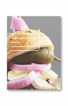 Showing stacked sandwich on wooden table with sesame bun, pickled onions, pepper spear and skewer