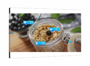 Displaying glass jar granola topped with blackberry and icons on kitchen board, with grapes