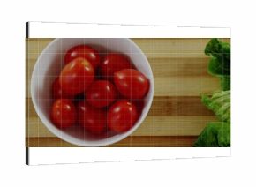 Displaying ceramic bowl holding red grape tomatoes on bamboo board on counter, with lettuce leaves