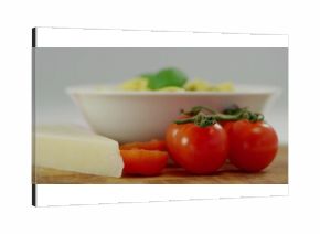Cluster and halved tomatoes resting atop cutting board in kitchen, with cheese wedge, pasta bowl