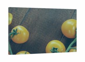 Displaying yellow cherry tomatoes on wooden kitchen tabletop, with green vines, halved tomato